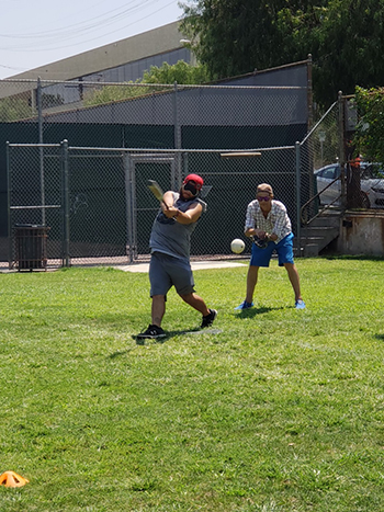 A male batter connects with the ball while his catcher waits on the ball behind him.
