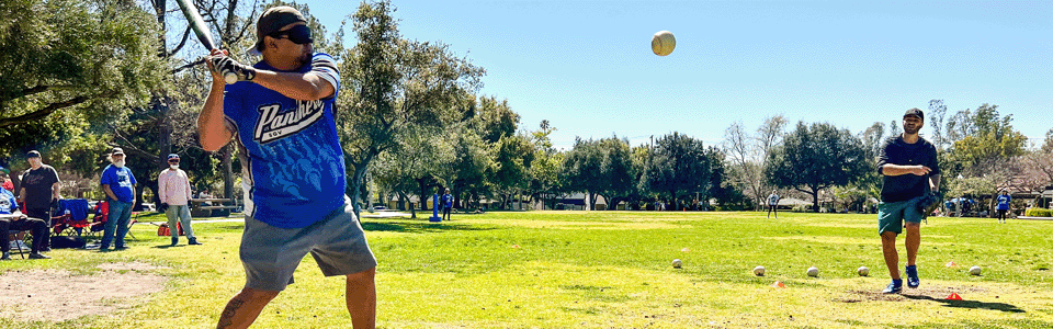 A SoCal player in batting stance as the pitcher hurdles a beep baseball toward him.